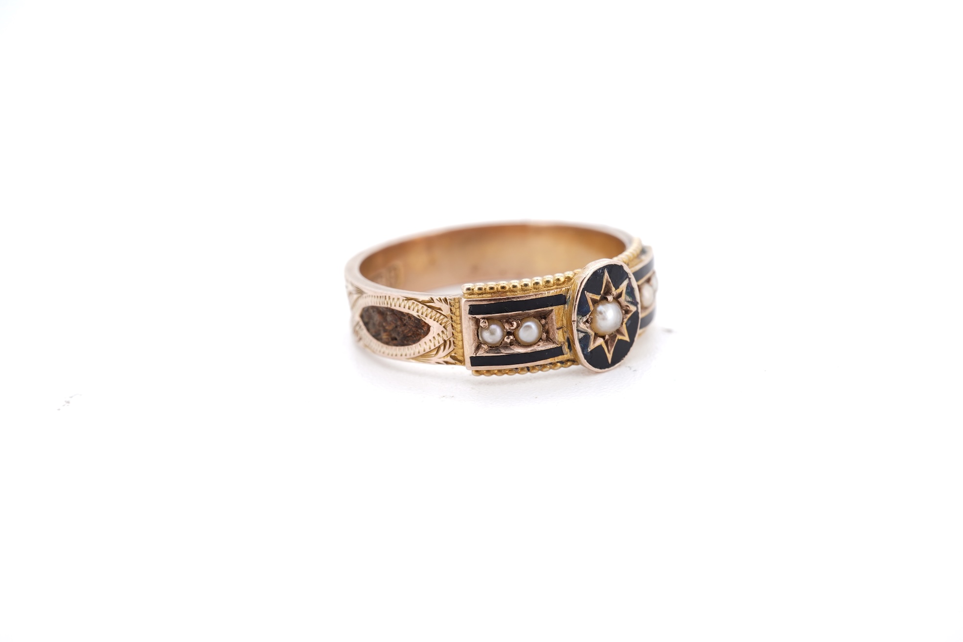 A George V 9ct gold, black enamel and seed pearl set mourning ring, the shank with panels of plaited hair, size O, gross weight 2.5 grams.